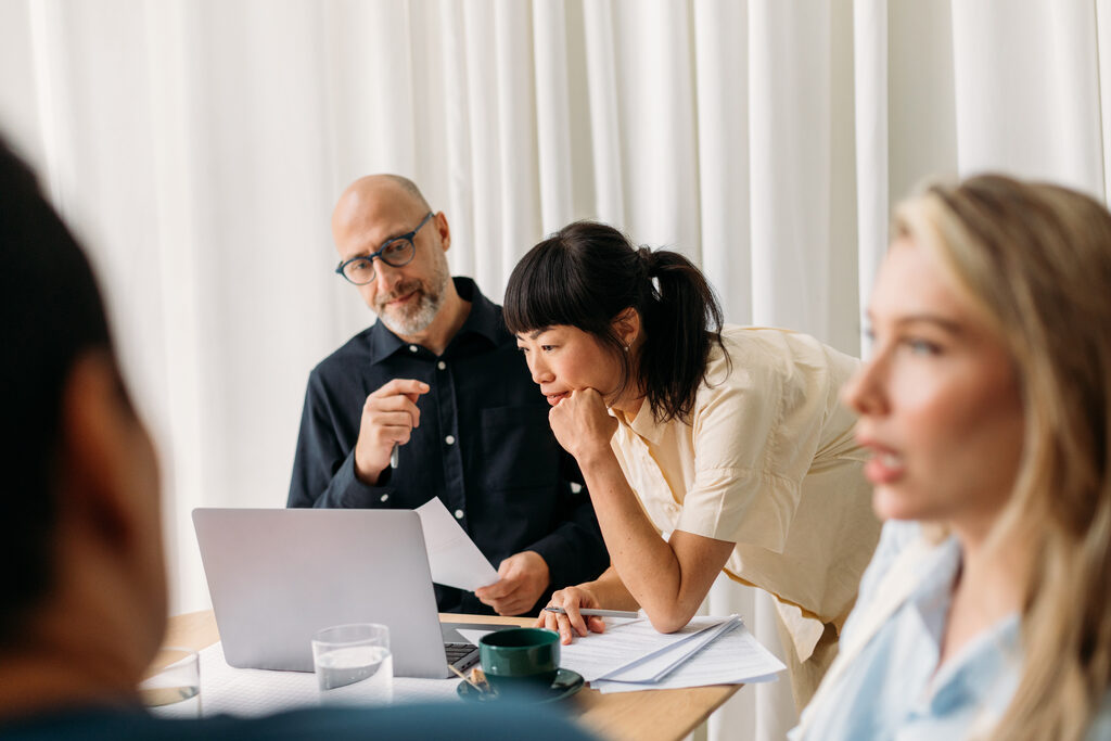 Colleagues gathered around a laptop, reviewing work together in a bright meeting room